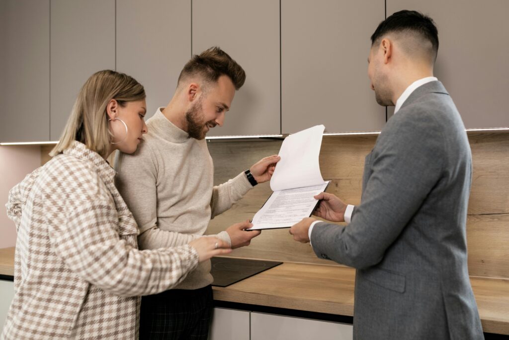 A couple reviews real estate documents with an agent in a modern indoor setting, discussing a potential property purchase.
